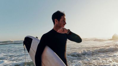 Surfista consultando su reloj inteligente en la orilla del mar al atardecer.