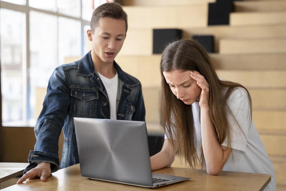 Dos jóvenes observan con gesto de preocupación y asombro la pantalla de un ordenador portátil en un interior.