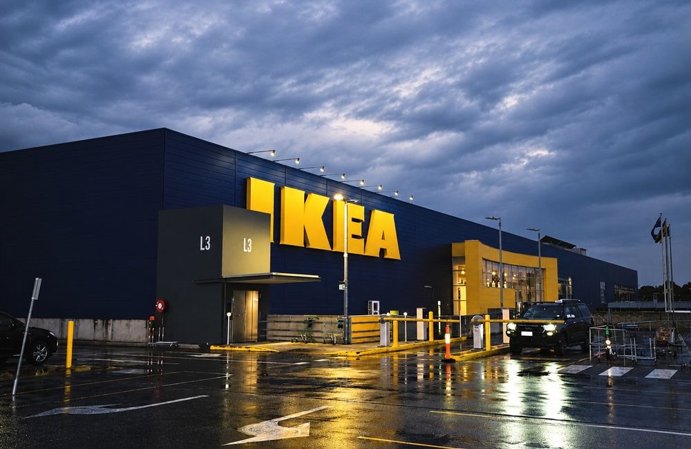 Fachada exterior de una tienda IKEA con su logotipo iluminado sobre el edificio azul bajo un cielo nublado.