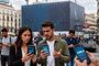 Personas en la Puerta del Sol de Madrid mirando sus teléfonos móviles con mensajes de falta de servicio de Movistar, O2 y DIGI.