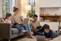 Familia de cuatro personas utilizando simultáneamente ordenadores portátiles y tabletas en un salón con un router WiFi al fondo.