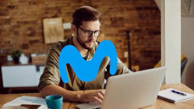 Hombre con gafas trabajando con un ordenador portátil frente al logotipo de Movistar superpuesto.