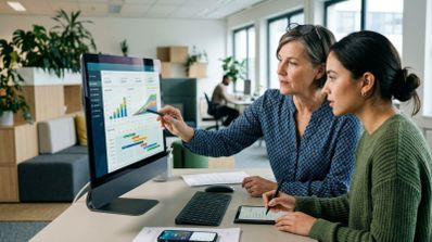 Dos compañeras de trabajo analizan un gráfico de crecimiento en la pantalla de un ordenador en una oficina.