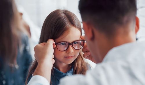 Niña probándose unas gafas graduadas con la ayuda de un óptico en una consulta profesional.