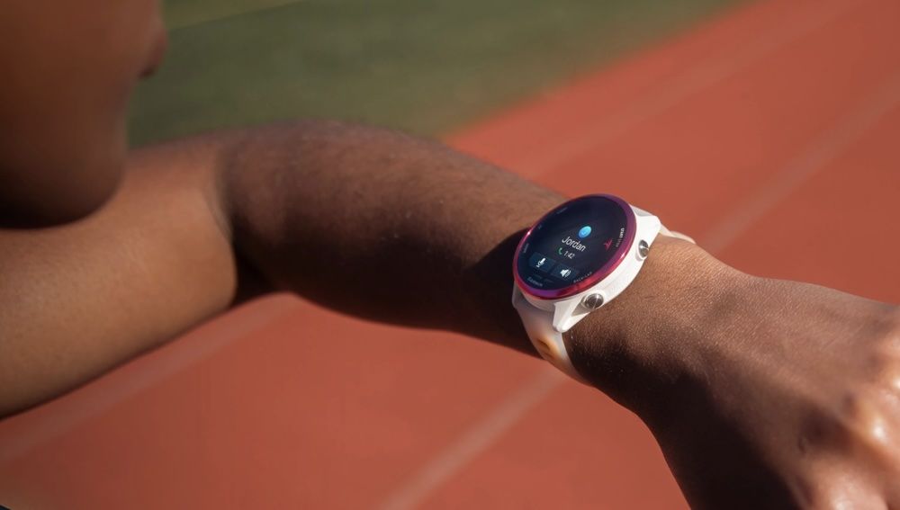 Primer plano de una persona consultando su reloj inteligente Garmin en una pista de atletismo.