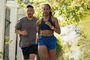 Pareja practicando running en una zona urbana con árboles y vallas de forja, la mujer luce un reloj inteligente en su muñeca izquierda.