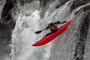 Persona descendiendo una cascada en un kayak de color rojo en aguas bravas.