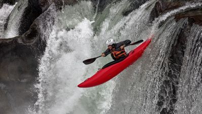 Persona descendiendo una cascada en un kayak de color rojo en aguas bravas.