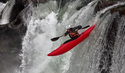 Persona descendiendo una cascada en un kayak de color rojo en aguas bravas.