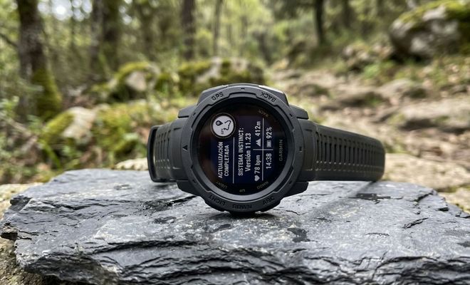 Reloj Garmin sobre una roca en el bosque mostrando un aviso de actualización completada en su pantalla.