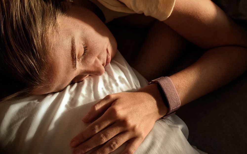 Mujer durmiendo en una cama con el dispositivo inteligente Garmin Cirqa en la muñeca para monitorizar el sueño.