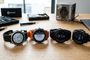 Cuatro relojes inteligentes Garmin Fenix alineados sobre una mesa de madera junto a herramientas de precisión y su caja original.