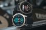 Dos relojes Garmin Fenix E con esferas digitales y correas negras en un entorno de gimnasio.