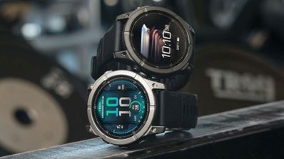 Dos relojes Garmin Fenix E con esferas digitales y correas negras en un entorno de gimnasio.