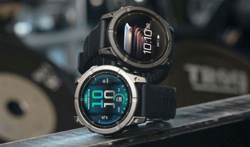 Dos relojes Garmin Fenix E con esferas digitales y correas negras en un entorno de gimnasio.