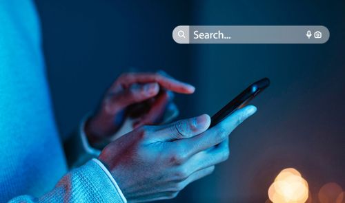 Persona utilizando un smartphone en un entorno con iluminación azulada junto a una barra de búsqueda digital.