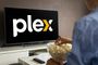 Persona de espaldas sentada frente a un televisor que muestra el logotipo de Plex mientras sostiene un cuenco de palomitas.