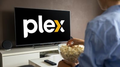 Persona de espaldas sentada frente a un televisor que muestra el logotipo de Plex mientras sostiene un cuenco de palomitas.