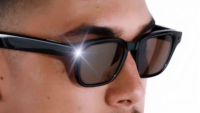 Detalle de una persona usando gafas inteligentes con una luz LED blanca encendida en el frontal de la montura.