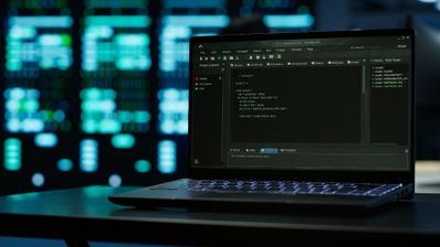 Ordenador portátil con editor de código abierto en pantalla ante un fondo desenfocado de centros de datos.