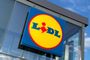 Logotipo circular amarillo y azul de Lidl instalado en una fachada de cristal bajo un cielo despejado.