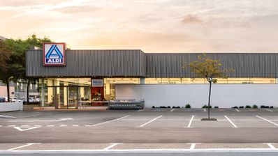 Fachada exterior de un supermercado Aldi con aparcamiento en primer plano al atardecer.