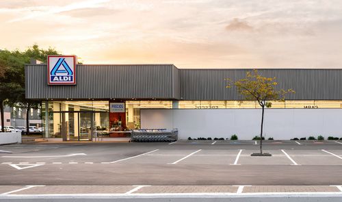 Fachada exterior de un supermercado Aldi con aparcamiento en primer plano al atardecer.