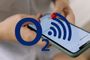 Primer plano de manos sosteniendo un smartphone con el logotipo de O2 y un símbolo de señal Wi-Fi superpuestos.