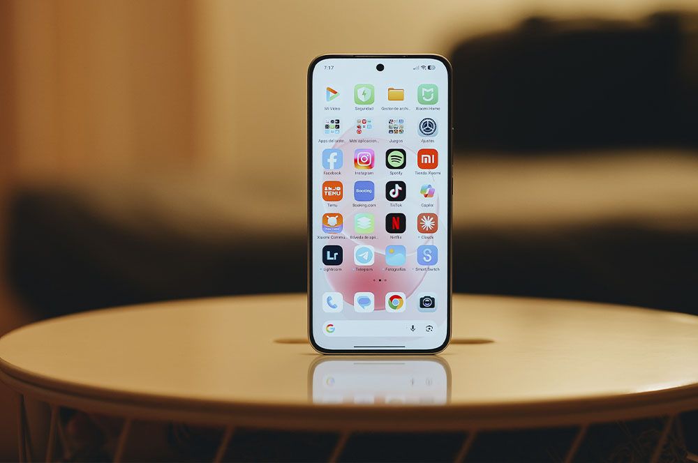 Primer plano del teléfono Redmi Note 17 Pro Max mostrando su pantalla de inicio con diversos iconos de aplicaciones sobre una mesa circular.