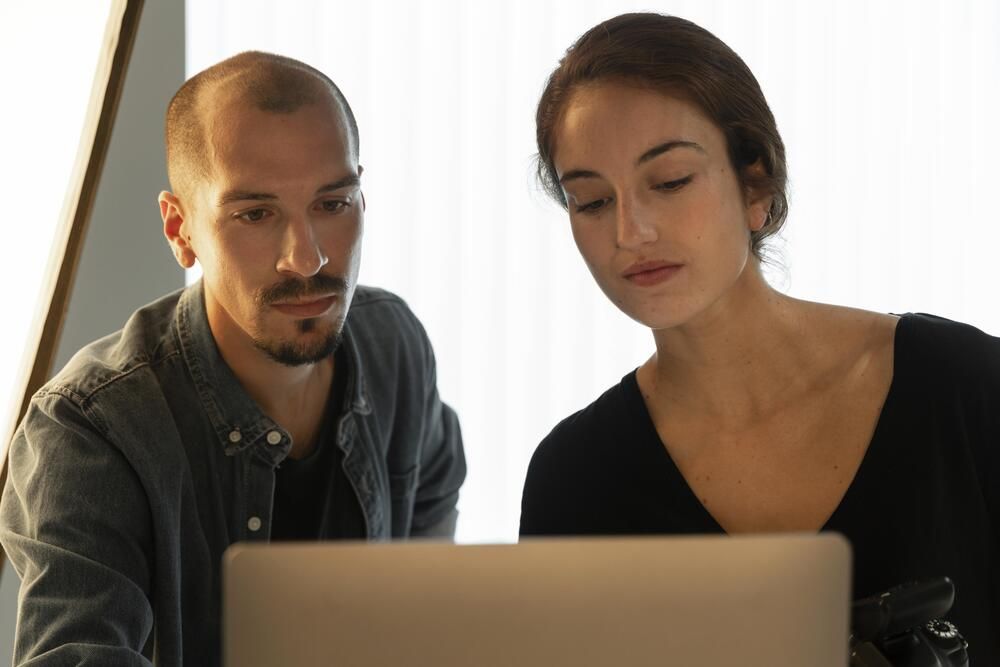 Dos personas jóvenes observando con atención la pantalla de un ordenador portátil en un espacio iluminado.