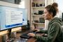 Mujer joven sentada frente a un monitor curvo descargando una actualización del sistema operativo en su escritorio.