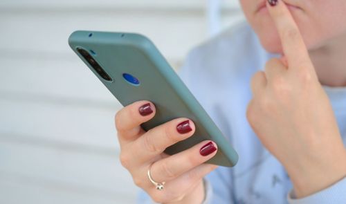 Primer plano de una persona sosteniendo un smartphone con funda verde mientras se lleva un dedo al rostro en actitud pensativa.