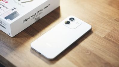 Vista trasera de un teléfono inteligente blanco con dos cámaras circulares junto a su caja sobre una mesa de madera.