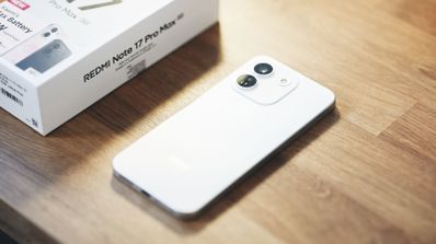 Vista trasera de un teléfono inteligente blanco con dos cámaras circulares junto a su caja sobre una mesa de madera.