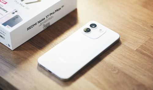 Vista trasera de un teléfono inteligente blanco con dos cámaras circulares junto a su caja sobre una mesa de madera.