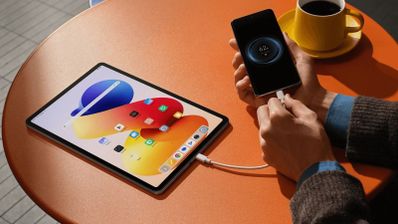 Tableta Redmi Pad Pro conectada mediante un cable USB a un teléfono móvil sobre una mesa naranja.