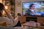 Mujer sentada en el sofá con el mando a distancia frente a una televisión con interferencias y píxeles en pantalla.