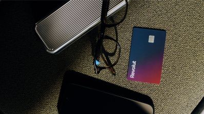 Tarjeta física de Revolut con degradado azul y morado situada junto a unas gafas y objetos personales sobre una superficie de tela.