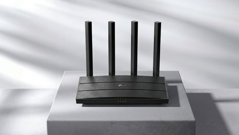 Router TP-Link de color negro con cuatro antenas verticales externas sobre un pedestal gris.