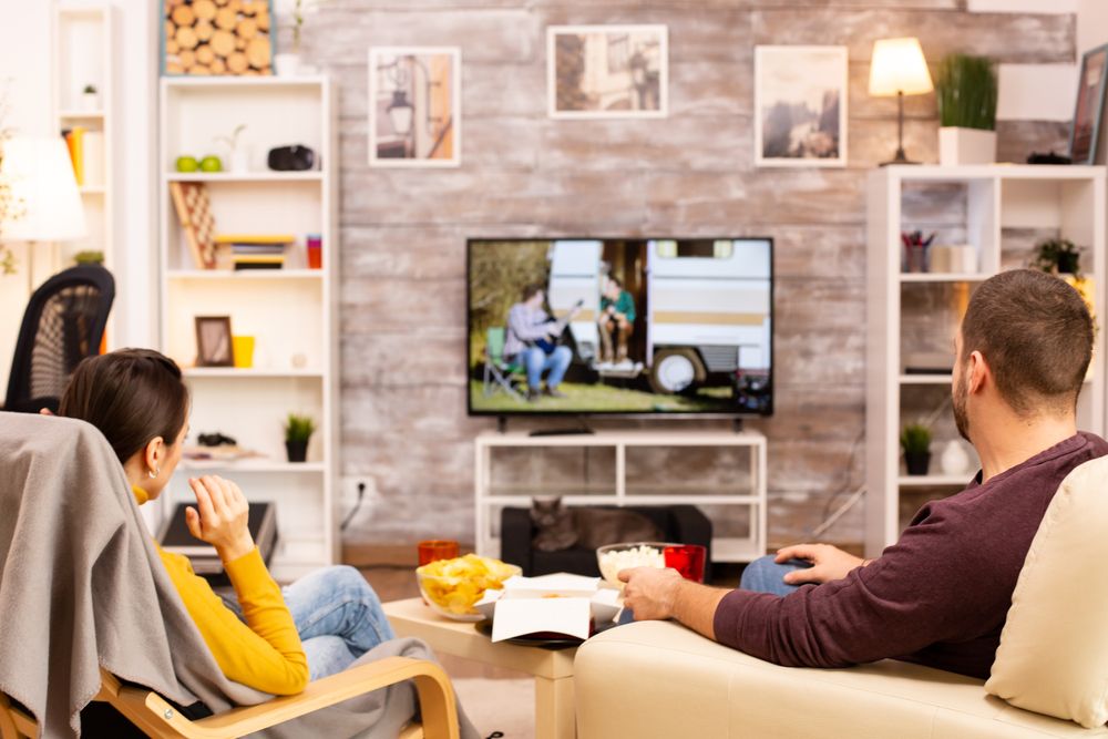 Pareja sentada de espaldas en un salón frente a una smart TV 4K que muestra una escena de acampada.