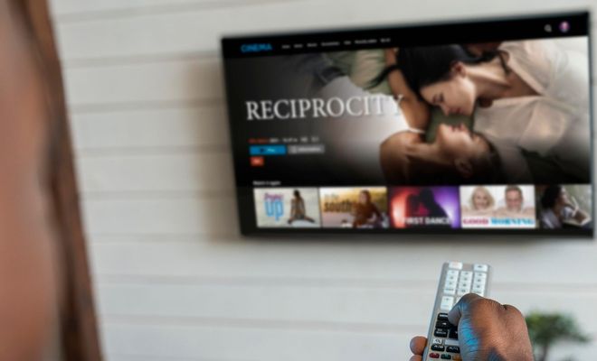 Primer plano de una mano sujetando un mando a distancia frente a una Smart TV con una interfaz de vídeo bajo demanda.