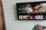 Primer plano de una mano sujetando un mando a distancia frente a una Smart TV con una interfaz de vídeo bajo demanda.