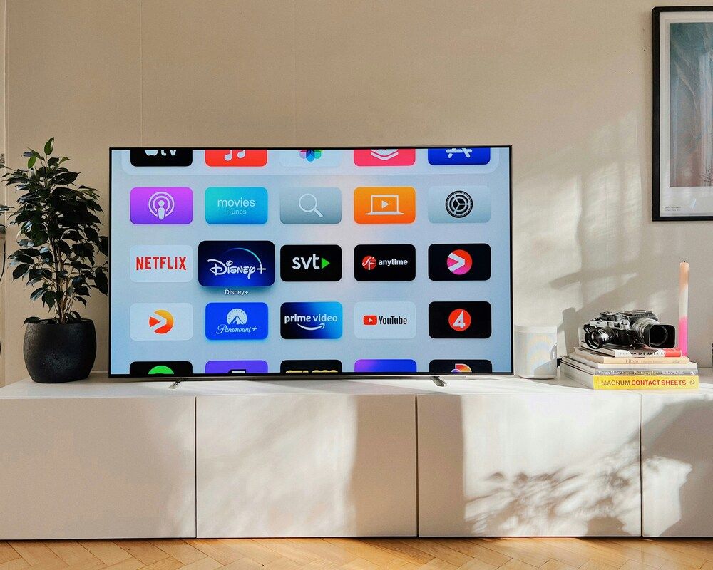 Smart TV encendida mostrando el menú de aplicaciones de streaming sobre un mueble blanco.