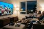 Familia sentada en el sofá viendo un documental marino en una Smart TV de gran formato rodeada de varios auriculares inalámbricos sobre la mesa y el reposapiés.