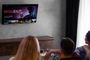 Tres personas de espaldas sentadas frente a una Smart TV colgada en la pared que muestra un menú de realidad virtual.