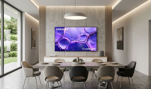 Televisor Samsung Crystal UHD instalado en la pared de un salón comedor moderno con iluminación cálida.