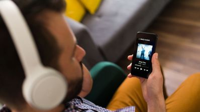 Primer plano de un hombre utilizando auriculares de diadema blancos mientras sostiene un smartphone con la aplicación Spotify abierta.