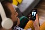 Primer plano de un hombre utilizando auriculares de diadema blancos mientras sostiene un smartphone con la aplicación Spotify abierta.