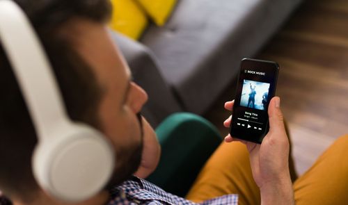 Primer plano de un hombre utilizando auriculares de diadema blancos mientras sostiene un smartphone con la aplicación Spotify abierta.