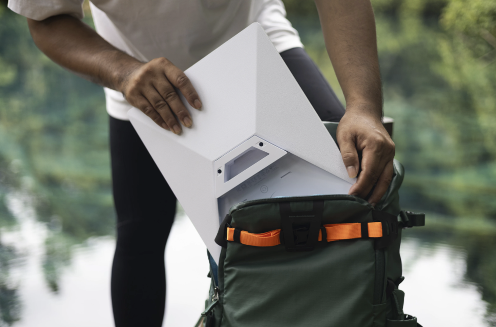 Persona guardando una antena plana rectangular de color blanco en una mochila de senderismo verde con correas naranjas.